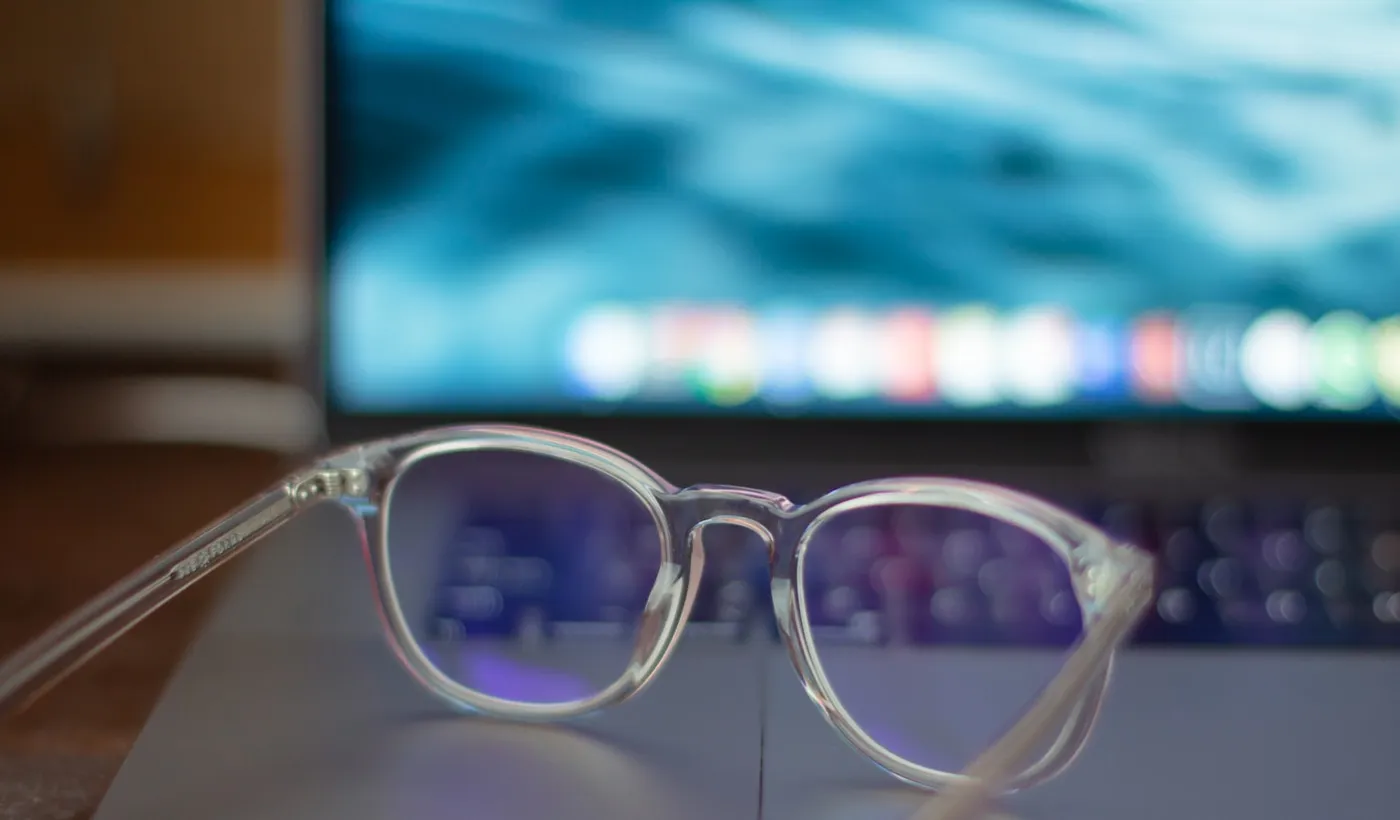 Silver-framed eyeglasses resting beside a computer workspace