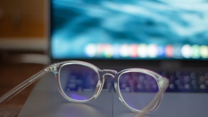 Silver-framed eyeglasses resting beside a computer workspace
