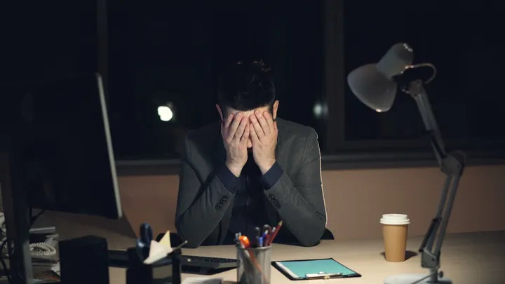 Person sitting at a desk with their head in their hands during a difficult workday