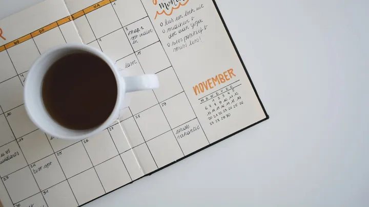 White coffee mug resting on an open planner used for cycle tracking
