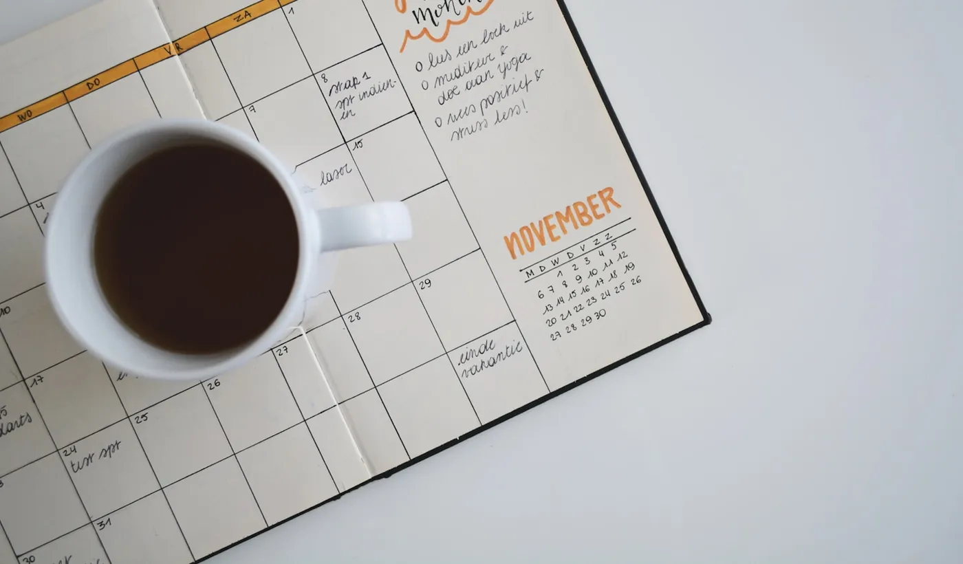 White coffee mug resting on an open planner used for cycle tracking