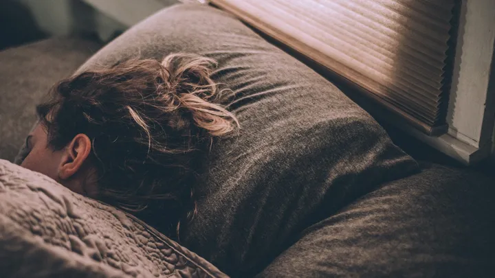 Woman sleeping under a white blanket in a dim bedroom