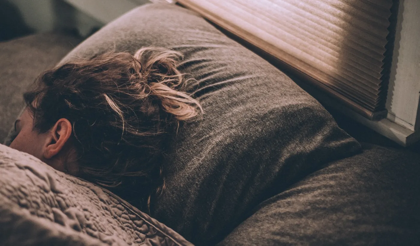 Woman sleeping under a white blanket in a dim bedroom